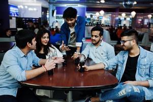 grupo de amigos asiáticos elegantes usam jeans sentados à mesa e bebem refrigerante de garrafas no clube. foto