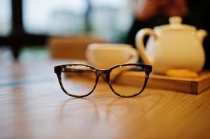 feche a foto de óculos contra a xícara de chá na mesa de café. conceito de óculos.