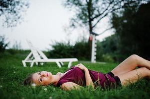 mulher sensual loira de vestido vermelho marsala, deitado na grama verde. foto