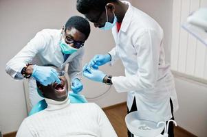 paciente de homem afro-americano na cadeira odontológica. consultório de dentista e conceito de prática médica. dentista profissional ajudando seu paciente na odontologia médica. anestésico de injeção. foto