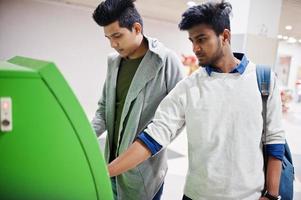 dois caras asiáticos retiram dinheiro de um caixa eletrônico verde. foto
