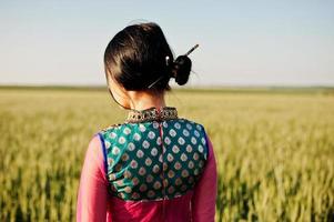 tenra garota indiana em saree, com lábios violeta compõem posou no campo no pôr do sol. modelo elegante da índia. foto