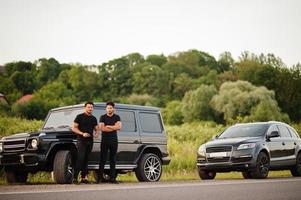 dois irmãos asiáticos vestem todo preto posando perto de carros suv. foto