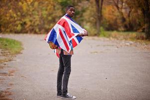 homem africano na camisa tradicional da África no parque outono com bandeira da Grã-Bretanha. foto