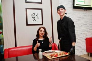 o desgaste do chef profissional em preto dá sushi e rolos para cliente mulher em um restaurante de comida tradicional japonesa. foto
