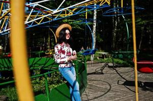 retrato de menina morena de óculos cor de rosa e chapéu com sorvete no parque de diversões. foto