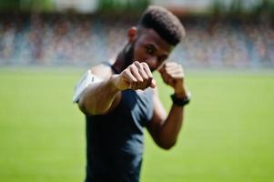 homem boxer atleta masculino americano africano em roupas esportivas fazendo alongamento no estádio. foto