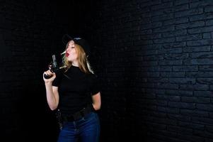 agente feminina do FBI no boné e com arma no estúdio contra a parede de tijolos escuros. foto