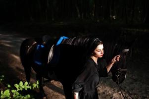 garota mística veste de preto com cavalo em madeira. foto