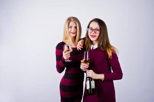 duas amigas atraentes em vestidos roxos bebem vinho espumante ou champanhe no estúdio. foto