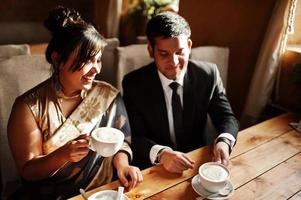 elegante e elegante casal de amigos indianos de mulher em saree e homem de terno sentado no café e bebendo cappuccino. foto