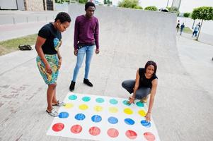 grupo de três amigos afro-americanos jogam o jogo twister ao ar livre. foto