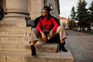 garota de moda afro-americana no casaco e boné de jornaleiro, óculos de sol posou na rua. foto
