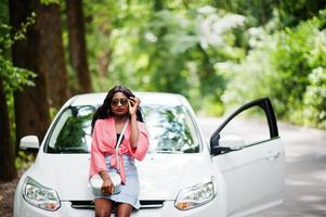 mulher afro-americana posou contra carro branco na estrada florestal. foto