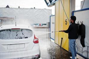 homem do sul da Ásia ou homem indiano lavando seu transporte branco na lavagem de carros. foto