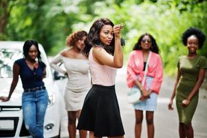 grupo de cinco garotas afro-americanas felizes posaram contra o carro, uma delas mostra as chaves. foto