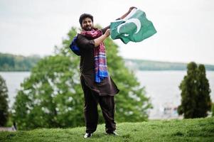 homem paquistanês usa roupas tradicionais segura a bandeira do paquistão. foto