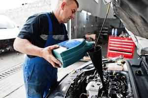 tema de reparação e manutenção de automóveis. mecânico de uniforme trabalhando em auto serviço, derramando óleo de motor novo. foto