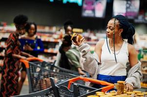 mulher afro-americana escolhe pote de mel no supermercado contra seus amigos afro com carrinho de compras. foto