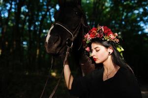 garota mística em grinalda veste em preto com cavalo em madeira. foto