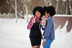 duas mulheres afro-americanas de cabelo encaracolado usam suéteres posados no dia de inverno, mostram dois dedos. foto