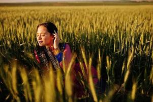 tenra garota indiana em saree, com lábios violeta compõem posou no campo no pôr do sol. modelo elegante da índia. foto