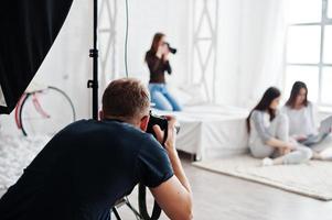 a equipe de dois fotógrafos atirando meninas de modelos gêmeos no estúdio que estão olhando para o laptop. fotógrafo profissional no trabalho. foto