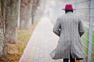 volta do modelo de homem afro-americano elegante ambulante com casaco cinza e chapéu vermelho. foto