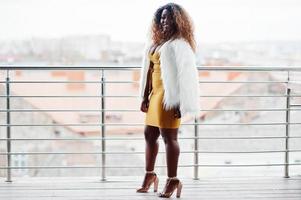 glamour mulher afro-americana de vestido amarelo e capa de lã branca posou na varanda. foto