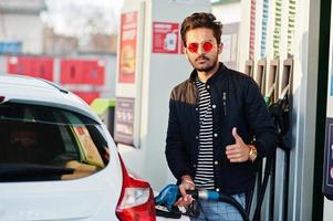 homem do sul da Ásia ou homem indiano reabastecendo seu carro branco no posto de gasolina. foto