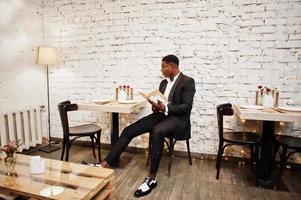 forte homem afro-americano poderoso em terno preto sentado no café e ler o livro. foto