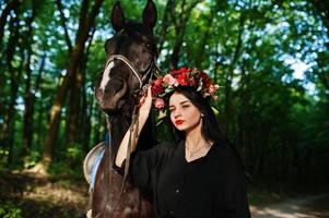 garota mística em grinalda veste em preto com cavalo em madeira. foto