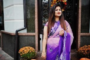 garota hindu indiana no tradicional saree violeta posou na rua contra a porta do restaurante com clima de outono e abóboras. foto