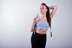 mulher de aptidão jovem atraente alegre em leggings top e pretas com pular corda e garrafa de água isolada sobre fundo branco. foto