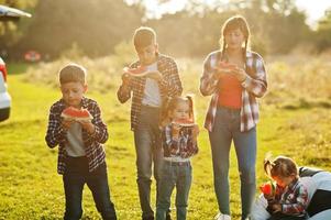 família passar tempo juntos. quatro filhos com mãe comem melancia ao ar livre. foto