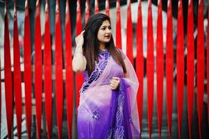 garota hindu indiana no tradicional saree violeta posou na rua contra um fundo vermelho. foto