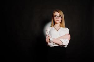 retrato de estúdio de empresária loira de óculos, blusa branca e saia preta contra um fundo escuro. mulher de sucesso e conceito de menina elegante. foto