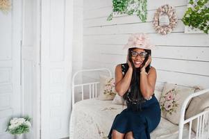 linda mulher afro-americana de óculos e chapéu posou no quarto sentado no sofá vintage. foto