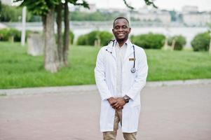 jovem médico americano africano de jaleco branco com um estetoscópio posado ao ar livre. foto