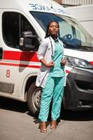 paramédico feminino americano africano em frente ao carro da ambulância. foto