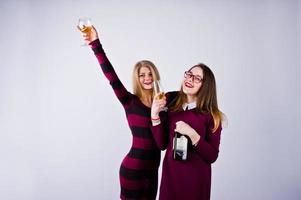 duas amigas atraentes em vestidos roxos bebem vinho espumante ou champanhe no estúdio. foto