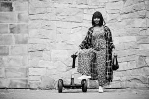 linda mulher afro-americana fica perto de segway ou hoverboard. garota negra com scooter elétrico de auto balanceamento de roda dupla. foto