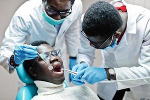 paciente de homem afro-americano na cadeira odontológica. consultório de dentista e conceito de prática médica. dentista profissional ajudando seu paciente na odontologia médica. perfurando os dentes do paciente na clínica. foto