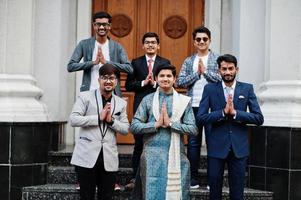 grupo de seis homens indianos do sul da Ásia em roupas tradicionais, casuais e de negócios em pé nas escadas e mostram o sinal de mãos namastê. foto