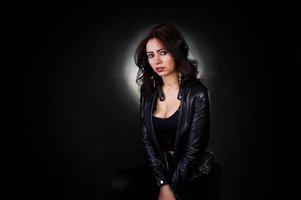 retrato de estúdio de menina morena sexy jaqueta de couro preta contra fundo preto. foto