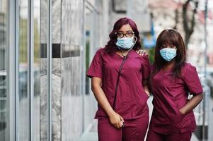 duas médicas afro-americanas em uniforme de laboratório vermelho em máscara facial protetora. conceito de medicina, profissão e saúde. pare a infecção por coronavírus. foto