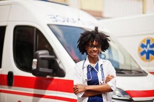 paramédico feminino americano africano em frente ao carro da ambulância. foto