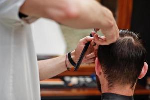 jovem barbudo cortando o cabelo pelo cabeleireiro enquanto está sentado na cadeira na barbearia. alma de barbeiro. foto