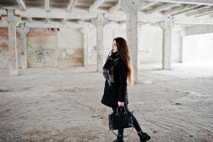 menina casual elegante morena no cachecol e bolsa contra fábrica abandonada. foto