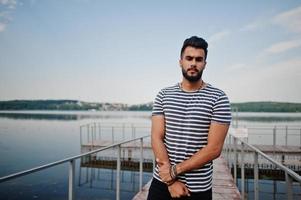 modelo de homem de barba árabe alto bonito na camisa despojada posou ao ar livre no cais do lago. cara árabe na moda. foto